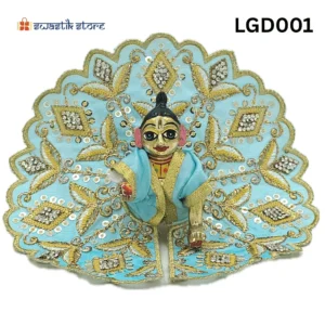 A small, brass Laddu Gopal (baby Krishna) deity idol is seated and dressed in a vibrant Light Blue poshak (outfit). The outfit is heavily adorned with intricate gold embroidery, silver sequins arranged in diamond patterns, and golden leaf-like designs. The deity has large, expressive eyes and a tilak on the forehead. The background is plain white, with a "Swastik Store" logo in the top left corner and the product code "LGD001" in the top right. - Swastik Store